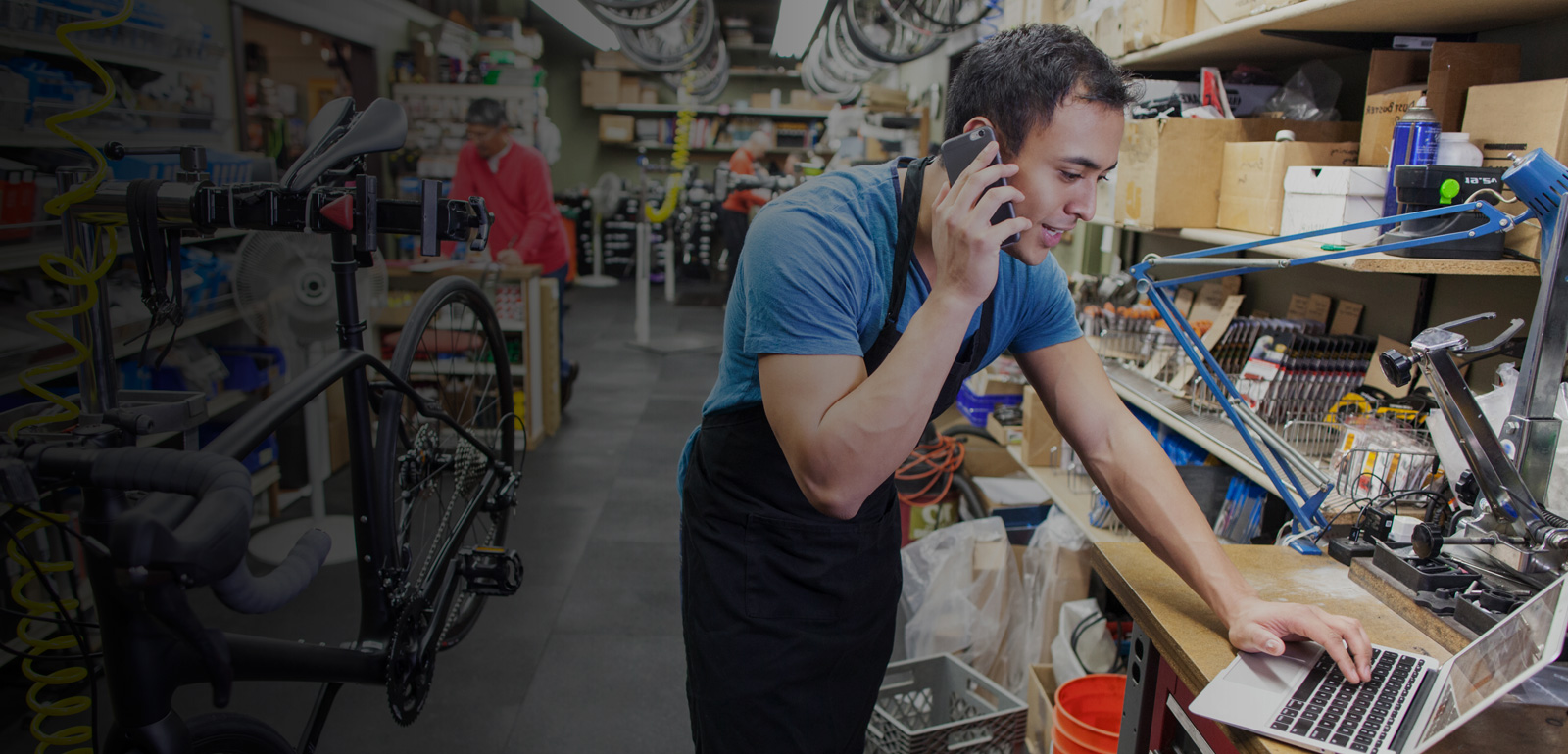 Man smiles while talking on the phone at a bike repair shop.