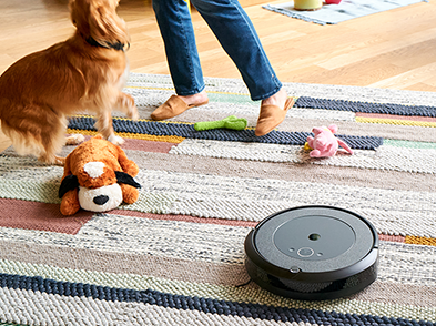 Person and dog on carpet behind a robotic floor cleaner
