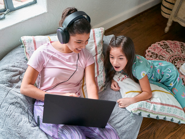 A mother and daughter watch a laptop screen while sitting on a bean bag chair