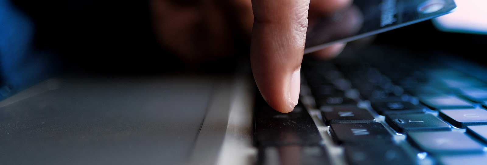 Single finger pressing down on a keyboard from above with the other hand holding a card  in the background
