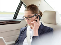 Woman in business suit and glasses with her hair in a bun talking on the phone from the backseat of a car 
