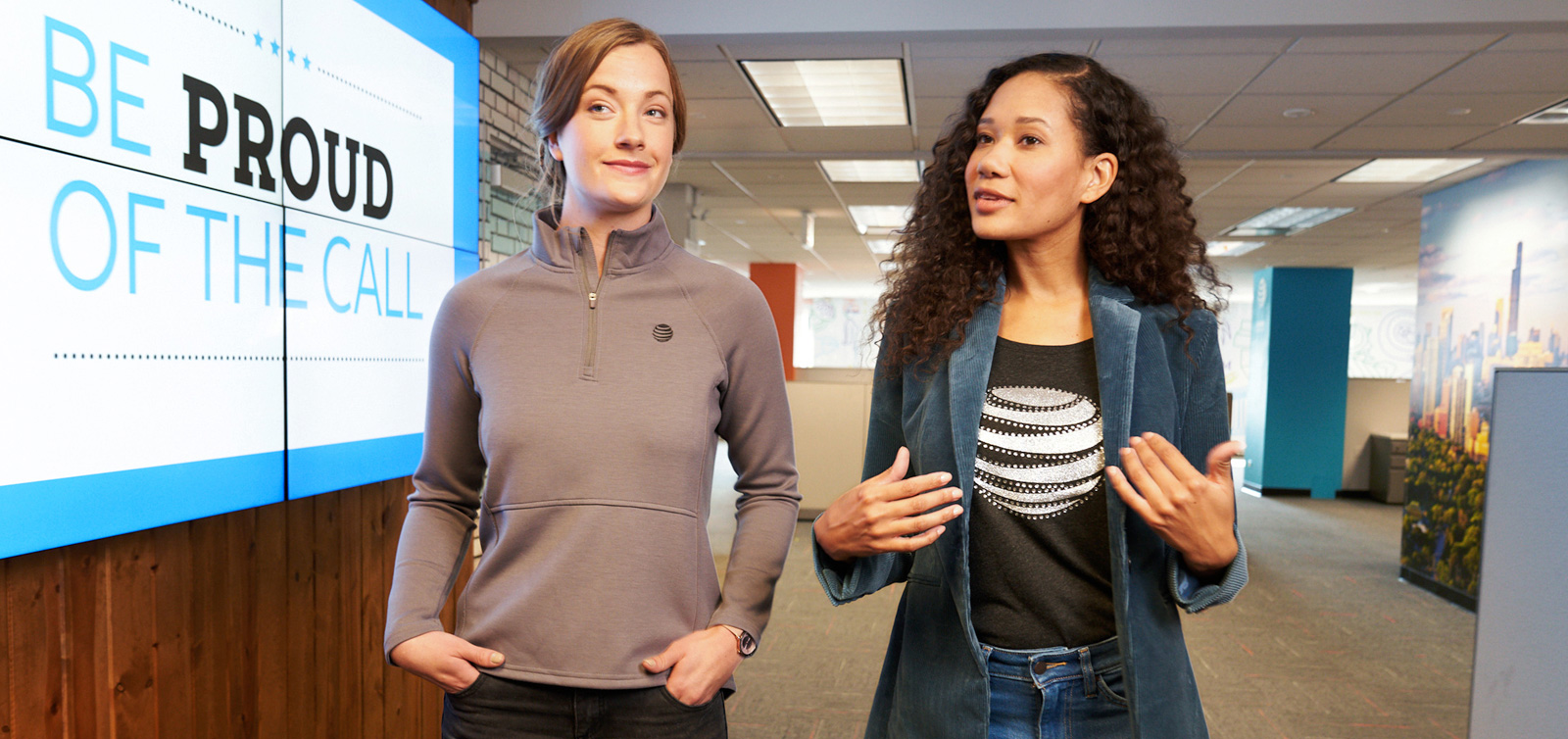 Two women walk and talk through an office hallway