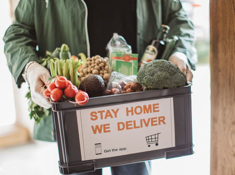 Person holding a bin full of food that says Stay Home We Deliver