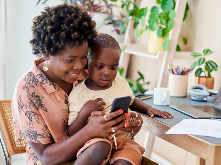 A mother and child look onto a smartphone screen smiling