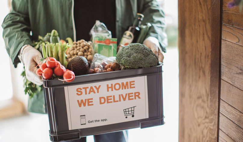 Person holding a bin full of food that says Stay Home We Deliver