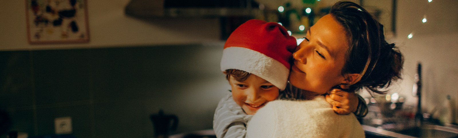 Son wearing Santa hat and hugging mom while standing in front of lights