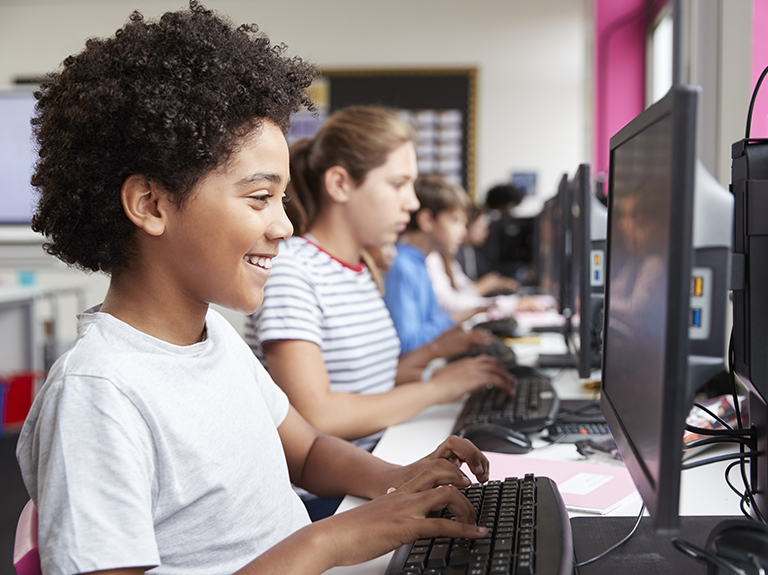 Children smile while using desktop computers at an AT&T Connected Learning Center 