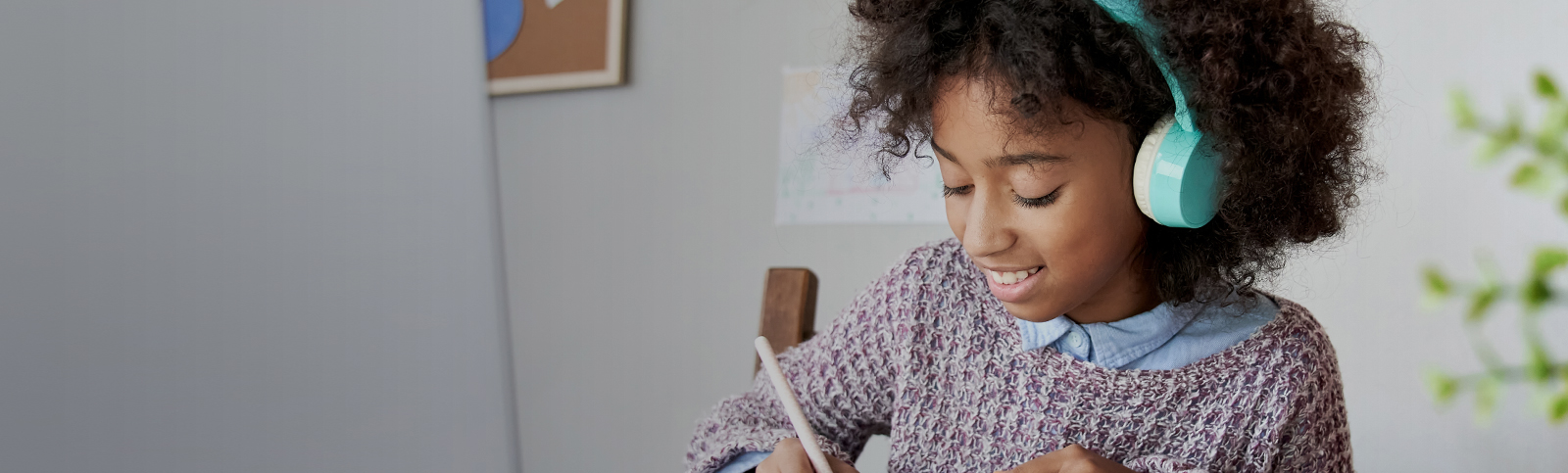 A schoolgirl smiles while writing with her Apple Pencil and listening to headphones 