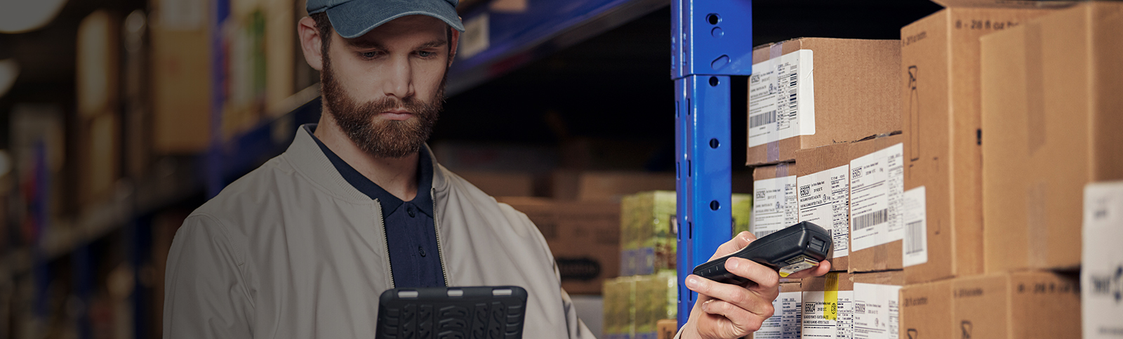 Man wearing blue hat in a warehouse scanning boxes with smart labels on his tablet