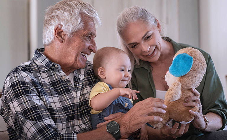 Grandparents wearing the Navigil 580 wellness wristwatch show off a stuffed toy to their grandchild