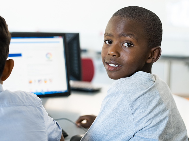 young boy smiling as he works on a computer