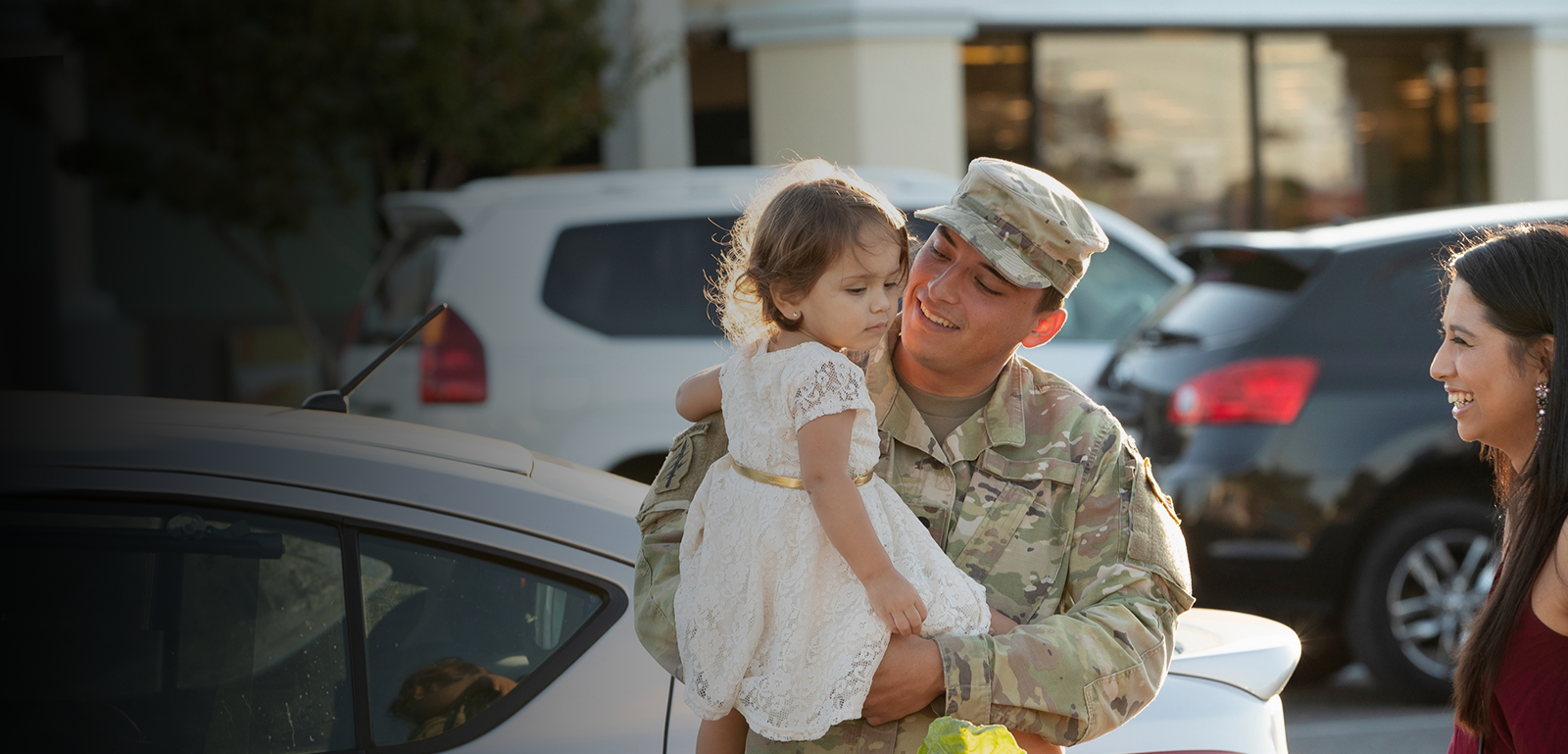 Military male holding his daughter in his arms as his wife smiles.