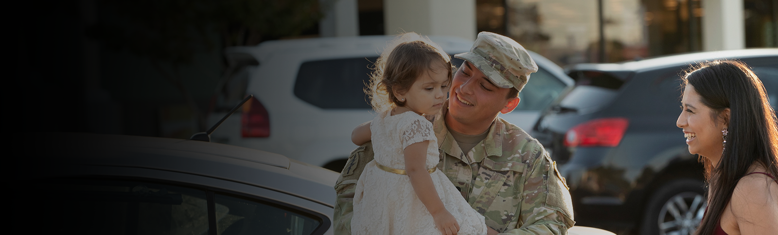 Military male holding his daughter in his arms as his wife smiles.