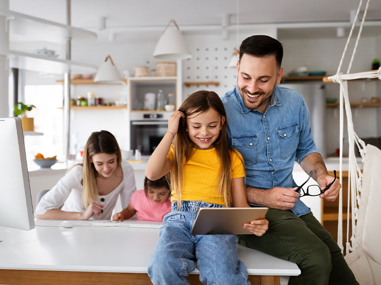 Family smiling using tablet and home computer.