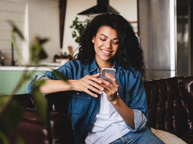 Woman sitting on couch, smiling at phone while answering phone call.