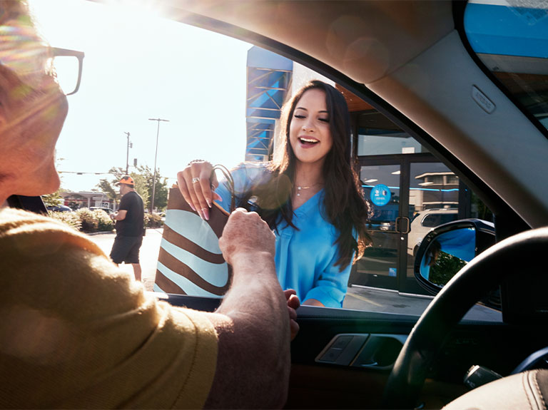 AT&T employee smiling, handing customer a shopping bag at curbside pickup.